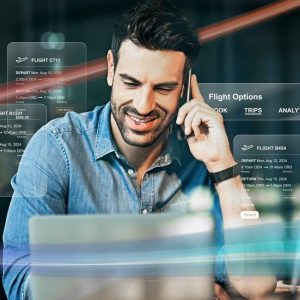 A man in front of a desktop computer, talking on the phone, preparing his travel program